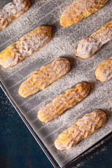Homemade Savoyardi cookies on a baking sheet on a blue background. Top view, flat lay.