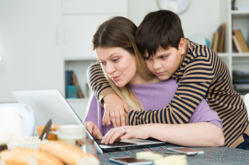 Young woman working at laptop with small son indoors