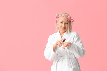 Mature woman in bathrobe and with bottle of cosmetics on color background