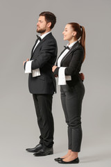 Male and female waiters on grey background