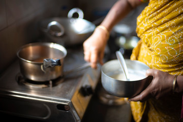 Tea being strained and poured into the cups from a steel tea pot in an Indian kitchen. Indian drink and beverages.