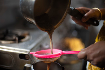 Tea being strained and poured into the cups from a steel tea pot in an Indian kitchen. Indian drink and beverages.