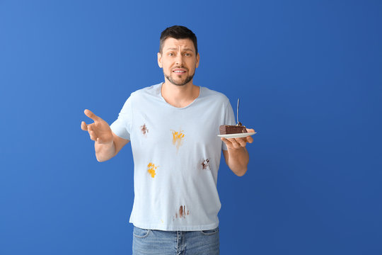 Displeased man in dirty clothes eating chocolate dessert on color background