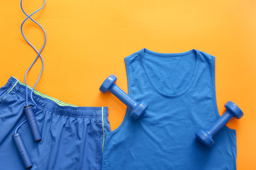 Sportswear and dumbbells on color background