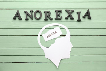 Word ANOREXIA and paper human head on wooden background