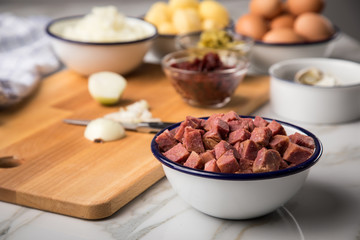 Zutaten  für Norddeutscher Hamburger Labskaus mit Rindfleisch Corned Beef, Rote Beete, Kartoffeln, Saure Gurken, Zwiebeln, Ei und Rollmops auf Marmor Arbeitsfläche
