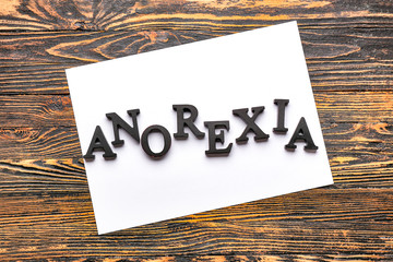 Word ANOREXIA and paper sheet on wooden background