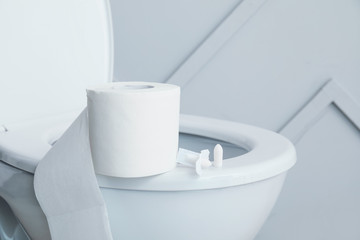 Toilet bowl with roll of paper and hemorrhoidal suppositories in restroom