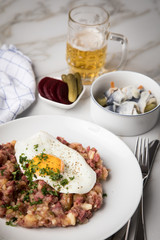 Norddeutscher Hamburger Labskaus mit Rindfleisch Corned Beef, Rote Beete, Kartoffeln, Saure Gurken, Spiegelei, Rollmops und Bier auf Marmor