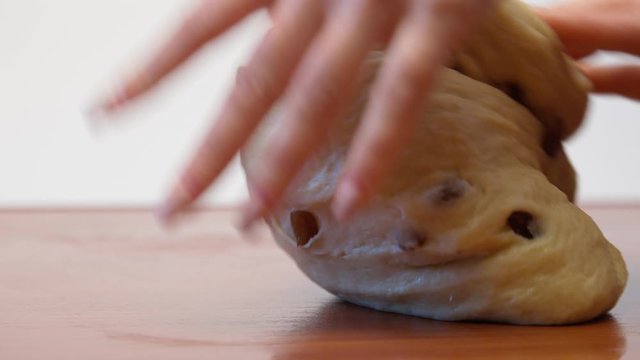 female hands knead the dough with raisins for panettone on the table. close-up
