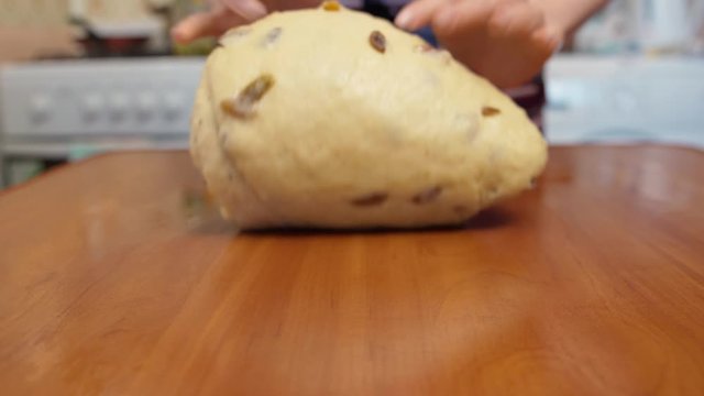 Woman kneads dough for panettone with hands on a wooden table in the kitchen, closeup.