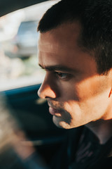 handsome brutal thin man with big brown eyes, clear skin, and rough stubble in a dark car and black clothes. bold portrait of a man close up. selective focus, mood toning