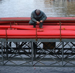 Construction worker with red pipes on a metal structure above water, Moika river, St. Petersburg, Russia, October 2019