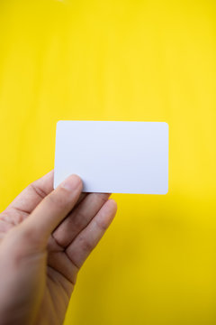 Close-up Of Person Hand Holding Blank Visiting Card Against Yellow Background