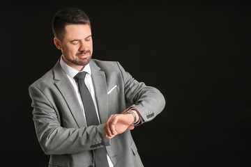 Portrait of handsome businessman looking at his watch on dark background