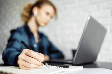 Blonde woman freelancer sitting at table with laptop, focus on hand