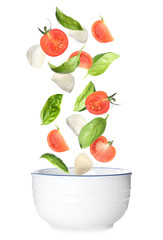 Mozzarella cheese balls, tomatoes and basil leaves falling into bowl on white background. Caprese salad
