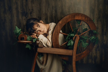 indoor portrait of young child girl with wool spinning wheel on wooden background