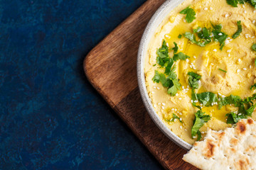 hummus on a plate with flatbread on wooden board, blue background