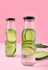 Bottles of cucumber infused water on color background