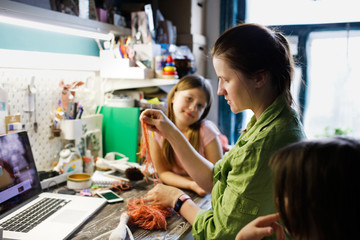mother sews dolls with kids in small home workshop