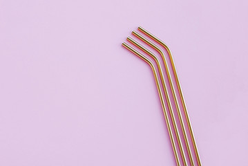 Reusable eco-friendly golden metal straws on pastel pink background.