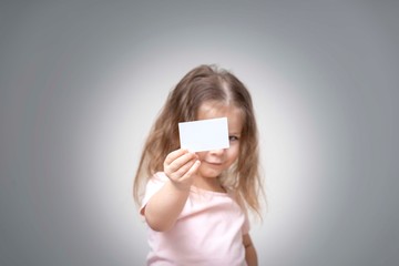 little girl holds a card in front of her and smile, portrait, copy space