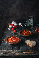 tomato soup in ceramic bowls with fresh basil leaves and bread slice on wooden background