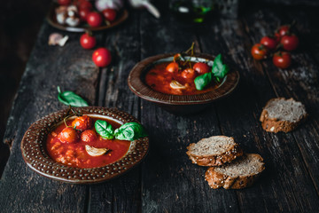 Fototapeta na wymiar tomato soup in ceramic bowls with fresh basil leaves and bread slice on wooden background