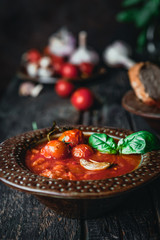 tomato soup in ceramic bowls with fresh basil leaves and bread slice on wooden background