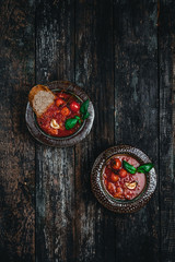 tomato soup in ceramic bowls with fresh basil leaves and bread slice on wooden background