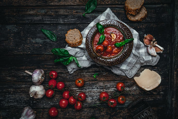 tomato soup in ceramic bowls with fresh basil leaves and bread slice on wooden background