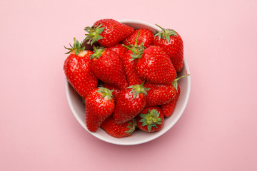 Fresh strawberries in a bowl on pink background.