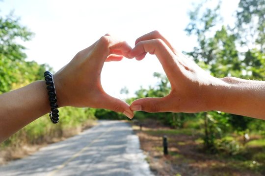 Close-up Of Couple Making Heart Shape With Hands Against Sky