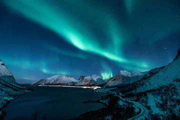 Poster poollicht ook wel noorderlicht of aurora borealis genoemd in het noorden van noorwegen in de winter boven een fjord en besneeuwde bergen © stalmphotos
