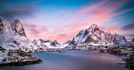 Obraz premium mountains and village of norway on the lofoten islands during winter while sunset and warm colors and blue sea