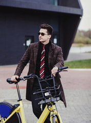 Young successful man in coat with bicycle in city