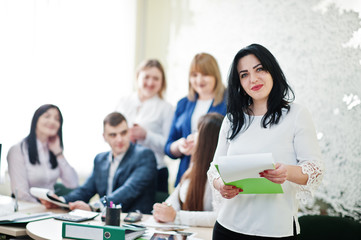 Portrait of caucasian woman in white blouse hold green folder against business people group of bank workers.