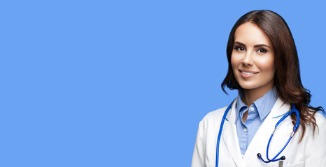 Portrait picture of happy smiling female doctor in white uniform coat and stethoscope, against blue color background. Healthcare, medical, medicine specialist - concept. Copy space.