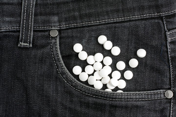 White pills lies in black jeans.