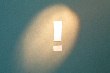 Exclamation mark cut out of paper on a textural green background highlighted by light