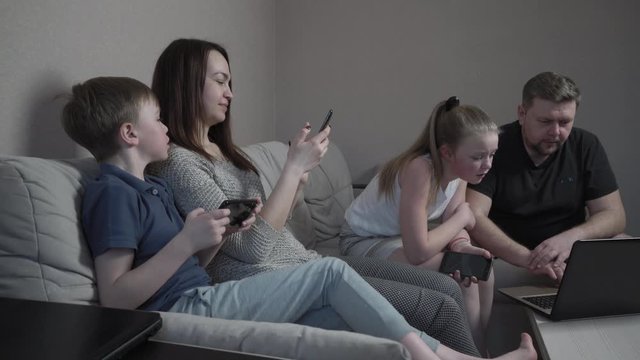 Family gloves using gadgets at home in isolation on coronavirus pandemic quarantine. Mom, dad, son and daughter watching film together on computer. Worldwide global COVID-19 epidemic.