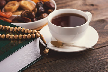 closeup cup of tea, plate of dried fruit, wooden rosary, Koran on brown wooden background, iftar, Ramadan