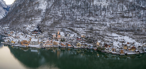 Aerial panoramic drone shot of Hallstatt village at foot of snow mountain by lake in Austria in winter