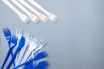 Forks made of wood and plastic on a gray background. Flat lay. Copy space. The concept of environmental pollution by difficult decomposable waste.