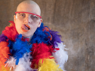 attractive girl with shaved bald head in a feather-cloak of LGBT colors. Beautiful middle-aged woman with cancer fell ill without hair in carnival cap LGBTQ