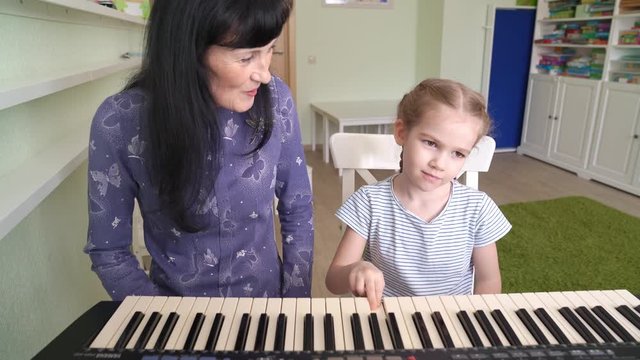 teacher teaches little girl to play on keyboard.