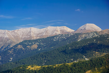View towards the main ridge of Pirin mountain in Bulgaria with Sinanitsa, Vihren and Koncheto peaks and autumn forest below them 
