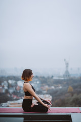 Woman practicing yoga on the mat on the roof and doing yoga exercises