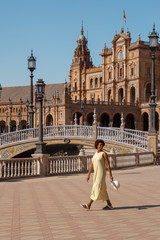 Naklejka premium afro american woman in plaza españa, sevilla. girl wearing a yellow dress and white hat